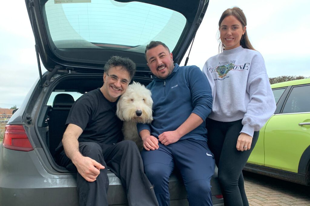 Professor Noel Fitzpatrick, an Old English Sheepdog and their family sitting in the boot of a car